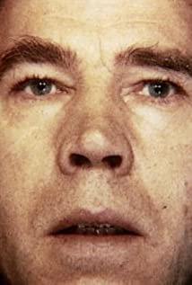 A close-up image of a man's face. He is staring into the camera and has a vacant expression on his face