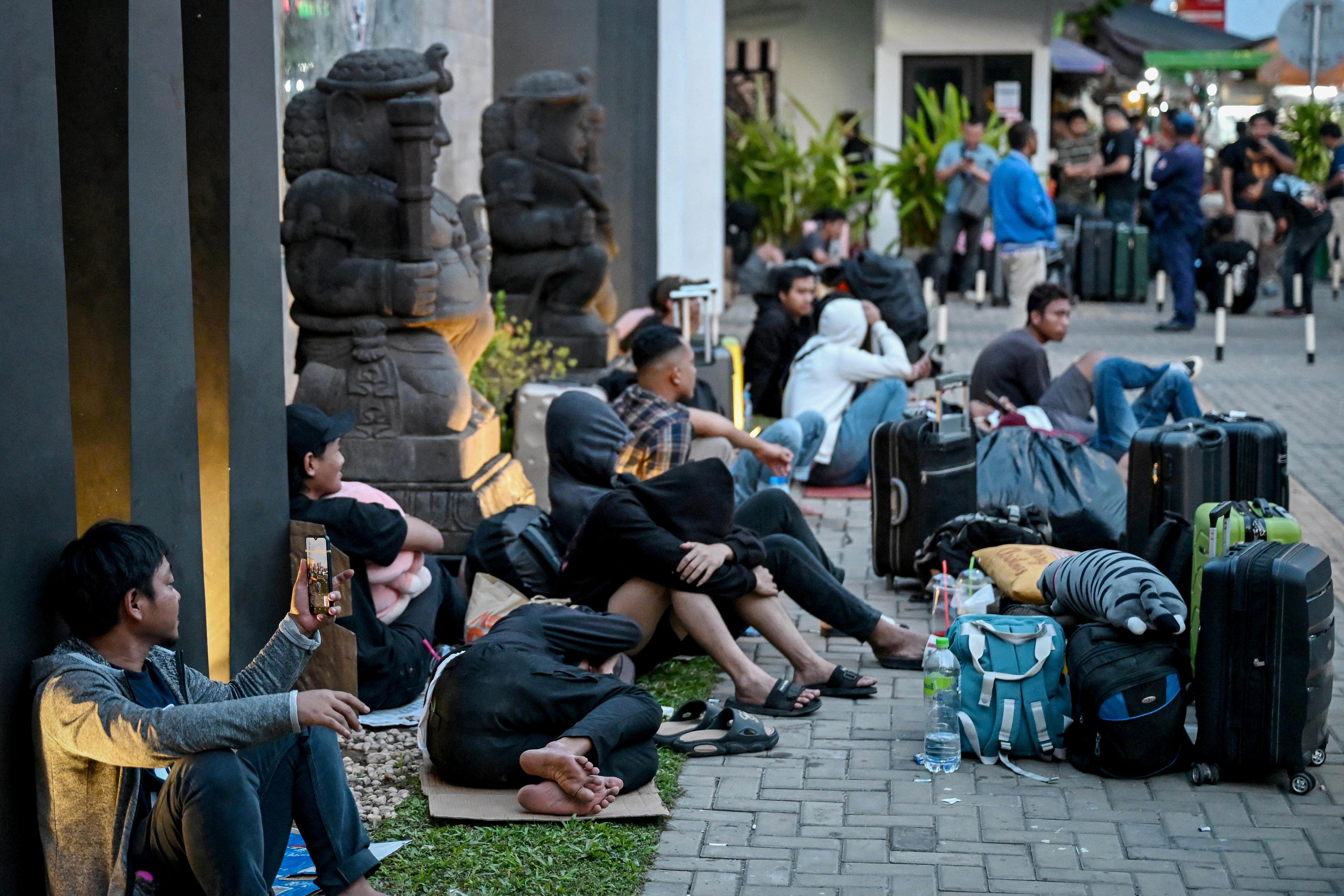 People sitting with luggage in the street in front of the Indonesian embassy in Phnom Penh.