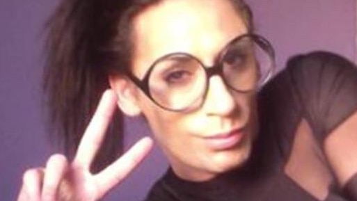 Transgender sex worker CJ Palmer, who is wearing glasses and has a ponytail, makes a peace sign at the camera.