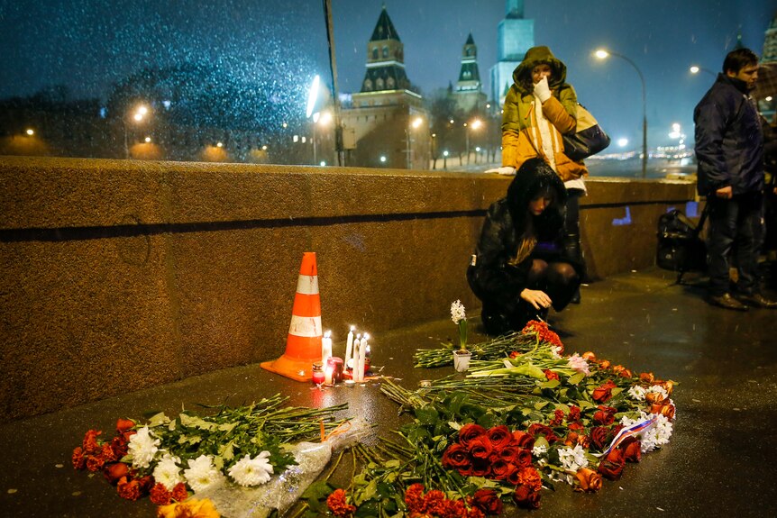 A woman crouches over a shrine of flowers and candles set up on a bridge at night