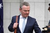 Christopher Pyne looks at the ground as he departs with a suit bag on his shoulder and brief case in his hand