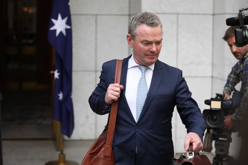 Christopher Pyne looks at the ground as he departs with a suit bag on his shoulder and brief case in his hand