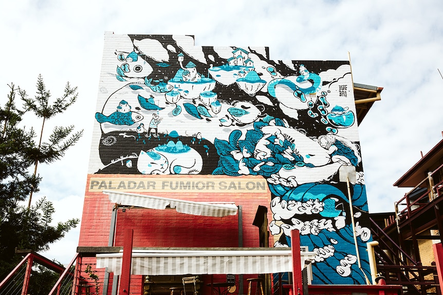 A blue, white and black mural on a brick wall.