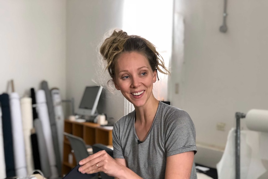 courtney lifts a piece of fabric off the cutting table at her studio