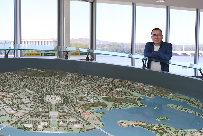 Man with glasses stands next to a design of Canberra.