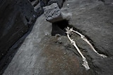 The legs of a skeleton emerge from the ground beneath a large rock believed to have crushed the victim's bust.