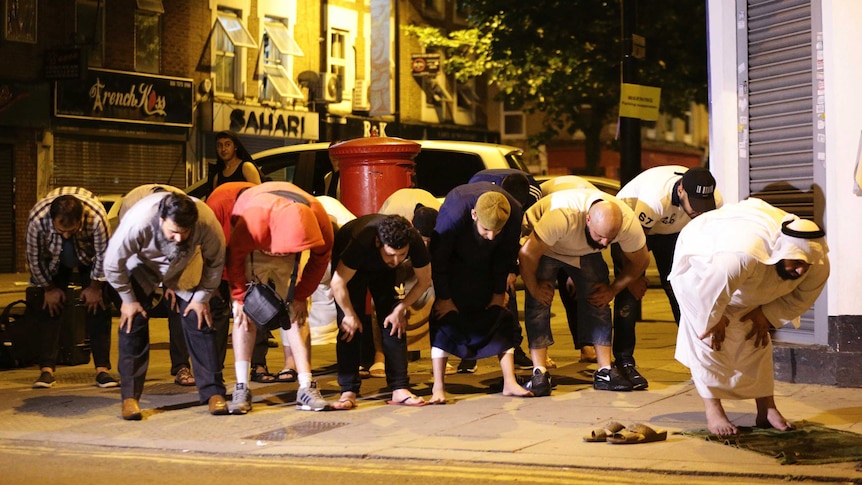 Several men bend at the hips in prayer in the street following an incident involving a van in Finsbury Park.