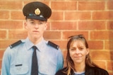 A young man in an airforce uniform standing next to a woman with shoulder length hair, in front of a brick wall.