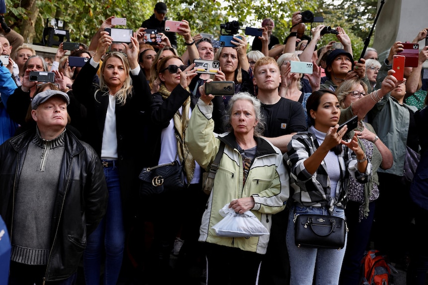 A crowd of people hold their smartphones up. 