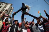 A group of around 10 men hold small Indian flags up as those in centre of group hold burning effigy representing Pakistan aloft.
