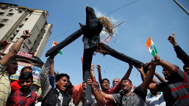 A group of around 10 men hold small Indian flags up as those in centre of group hold burning effigy representing Pakistan aloft.