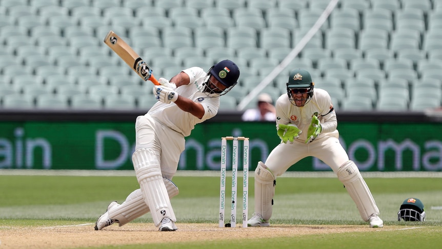 A batsman swings his bat above his head with a wicketkeeper standing up to the stumps