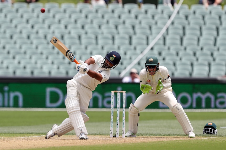 A batsman swings his bat above his head with a wicketkeeper standing up to the stumps