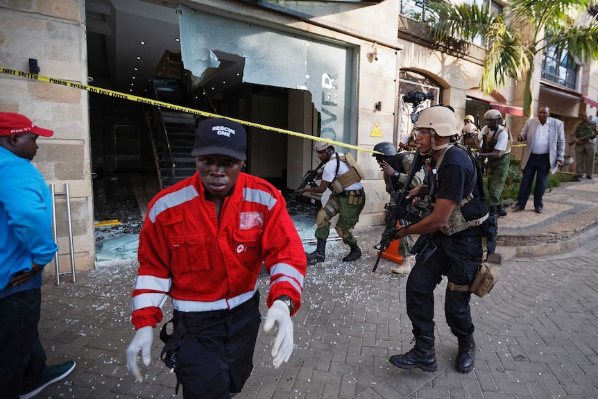 Security forces surround a hallway behind a shattered door in which an unexploded grenade lies.