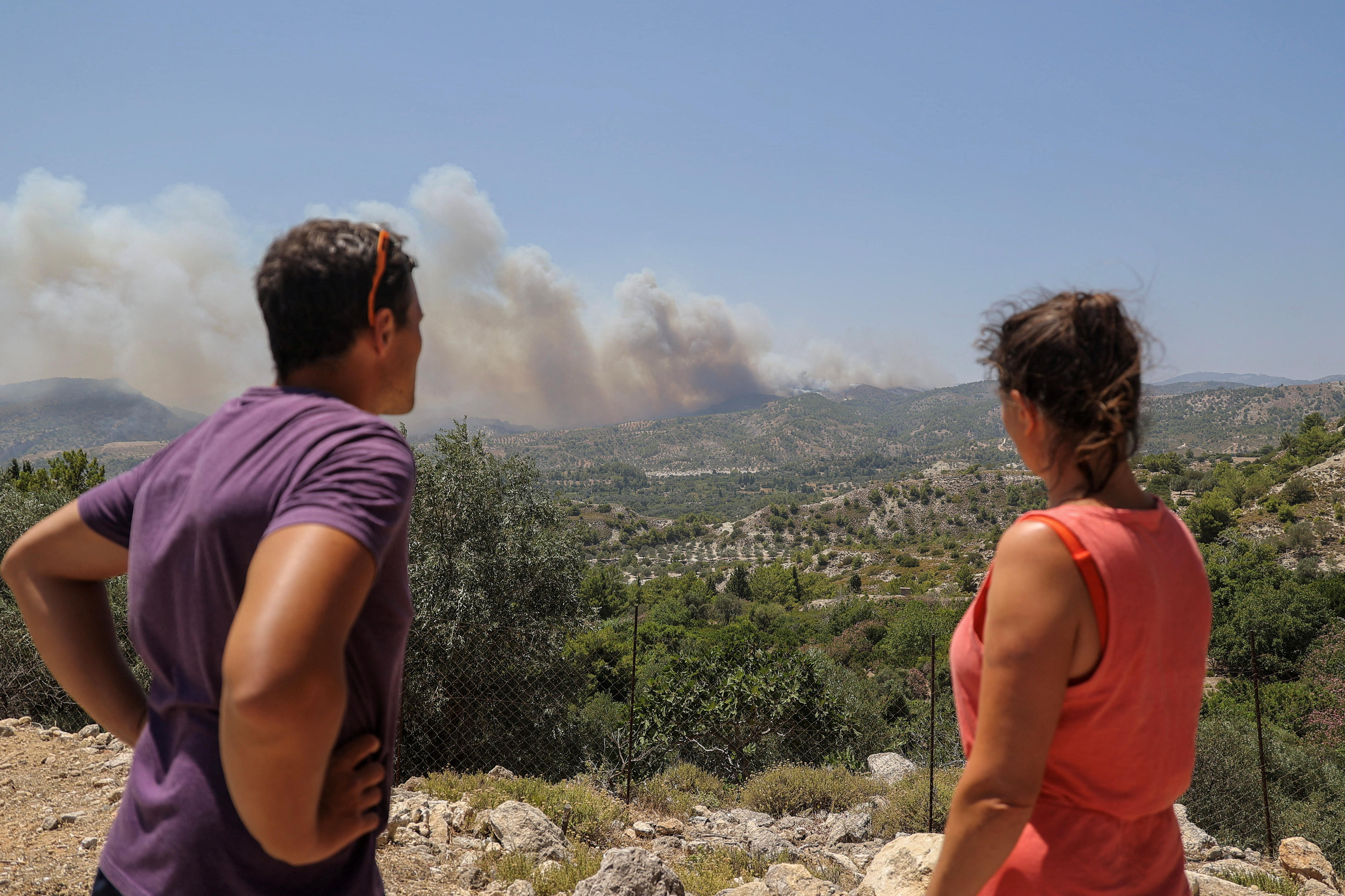 The back of a man and a woman looking out across a ledge where smoke burns