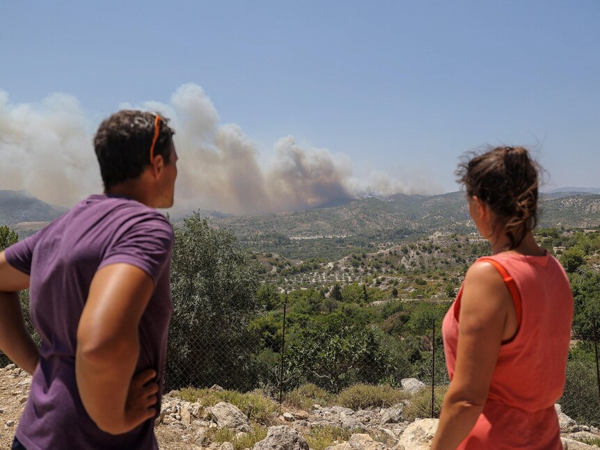 The back of a man and a woman looking out across a ledge where smoke burns