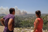 The back of a man and a woman looking out across a ledge where smoke burns