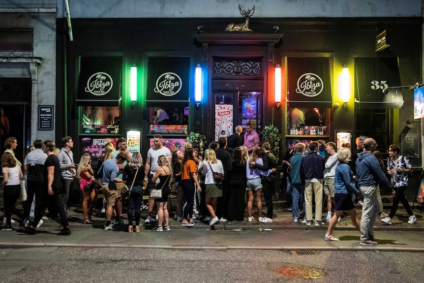 A crowd on a foodpath outside a bar with signs saying "Ibiza".