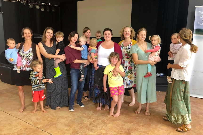 A group of mums and their children standing in a community hall.