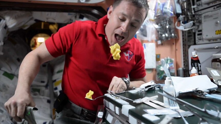 Astronaut within the International Space Station trying to eat his floating pudding