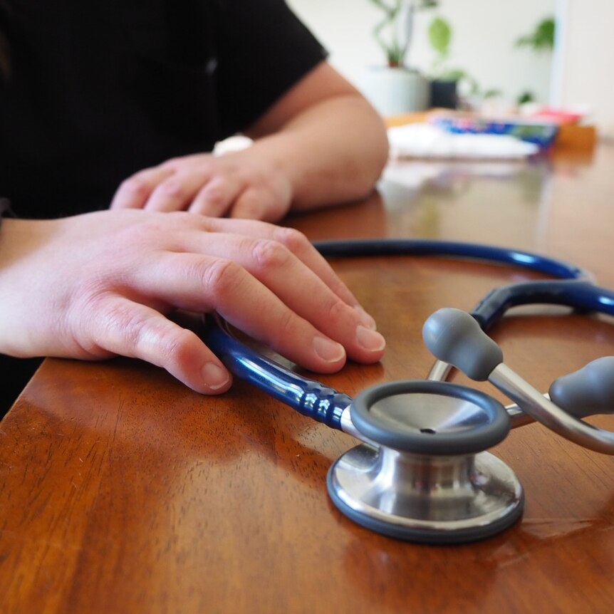 Anonymised pic of a doctor's hands at a desk holding a stethoscope