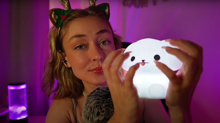 A young woman in a softly lit room holds a glowing plastic toy.