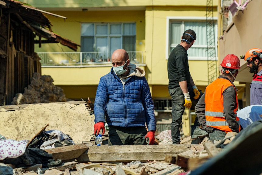 A man in a mask stands in rubble 