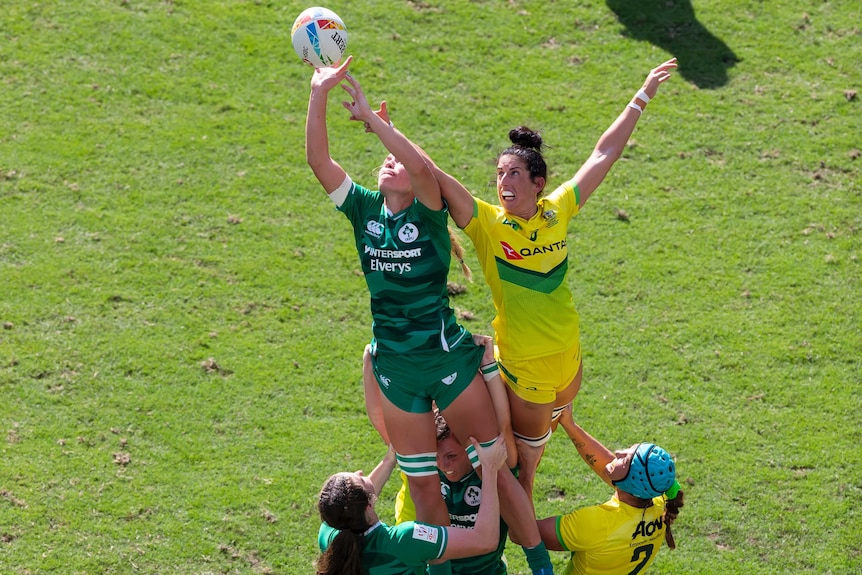 Two rugby players lifted in the air, stretch their arms out to try to take the ball in a lineout.