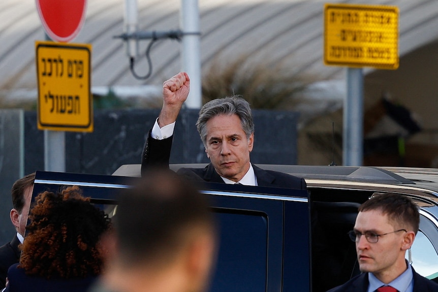 Antony Blinken gestures to a crowd by holding his fist in the air as he steps into a car
