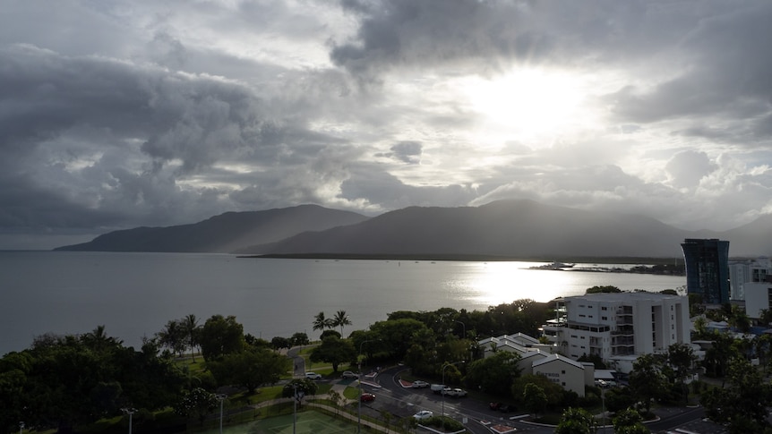 Sun shining through clouds over hills and water behind the Cairns skyline