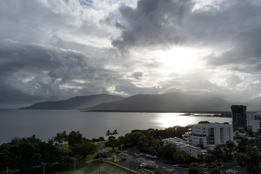 Sun shining through clouds over hills and water behind the Cairns skyline