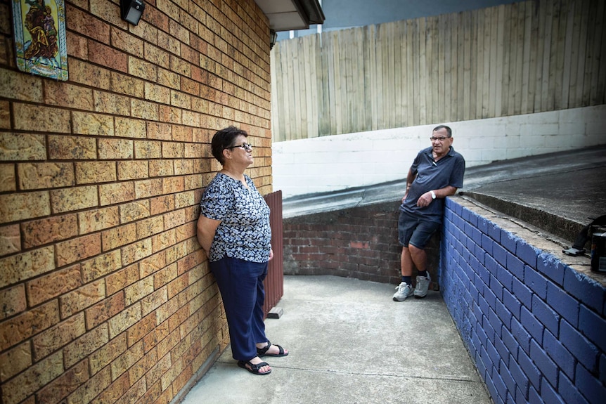 A woman leans against a wall and a man does the same.