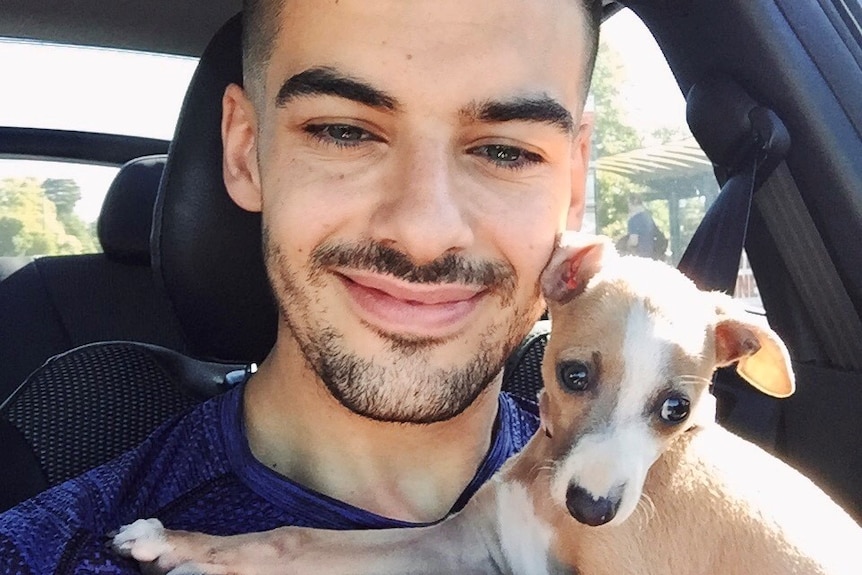 Harry Verveniotis smiles as he looks into the camera holding Lucia, who is across his chest. He wears blue and is in a car.