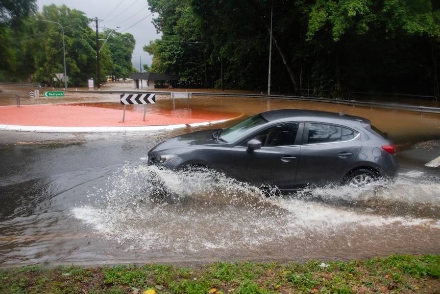 a medium-sized car drives through a flooded roundabout in cairns