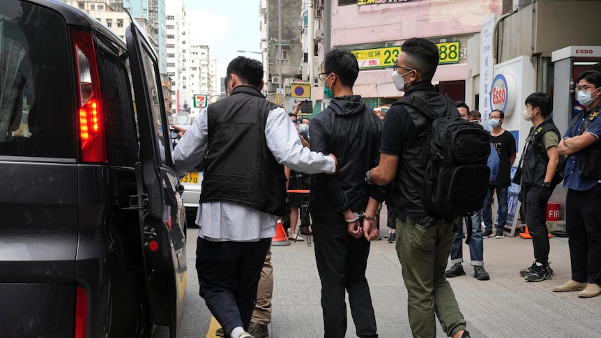 A man is led by two plain clothed police officers into an unmarked car