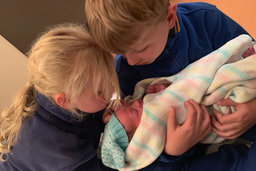 Newborn baby Quinn is held by his two older siblings.