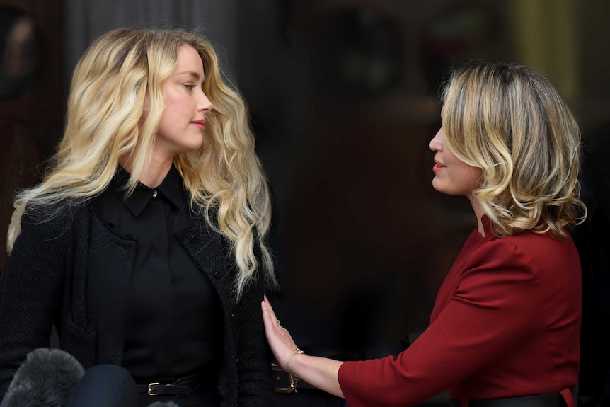 A blonde woman wearing black looks across at a woman in a red suit