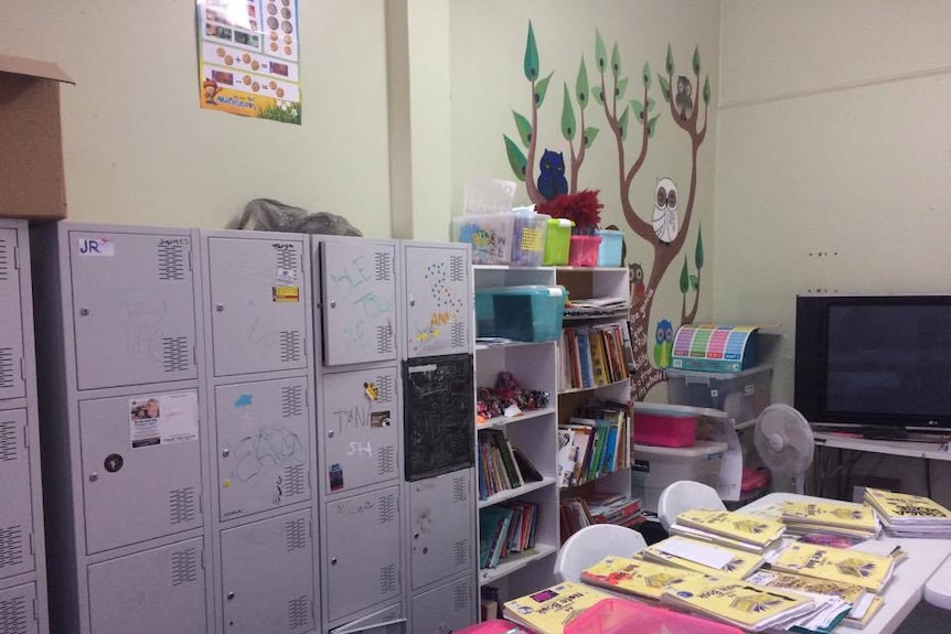 Lockers with writing on them on the left, with A4 note books spread out on the table. A TV in shot and owls on a tree as artwork