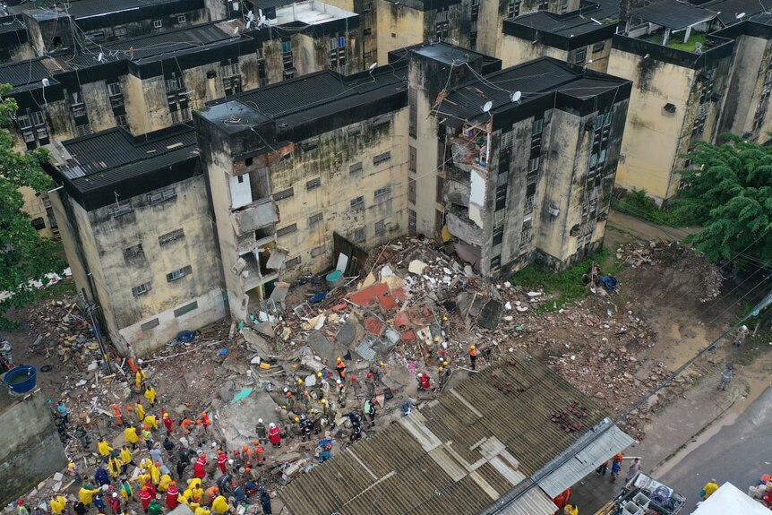 A collapsed building from aerial view with rescue workers standing arond. 