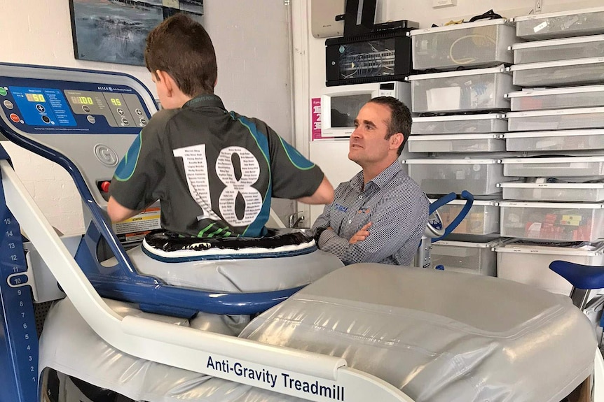 A young boy uses an anti-gravity treadmill as a professional supervises.
