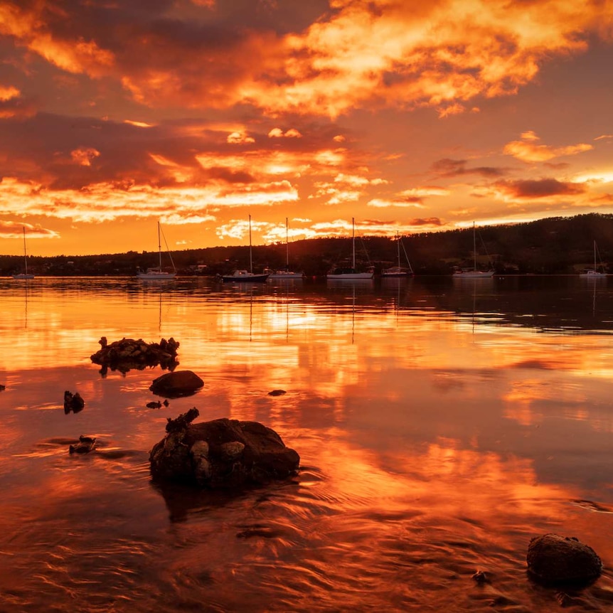 Sunset reflected in still bay waters, with a hill on the horizon.