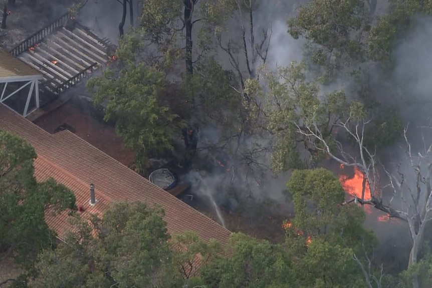 A property owner uses a hose to try defend their home after the fire destroyed multiple nearby properties