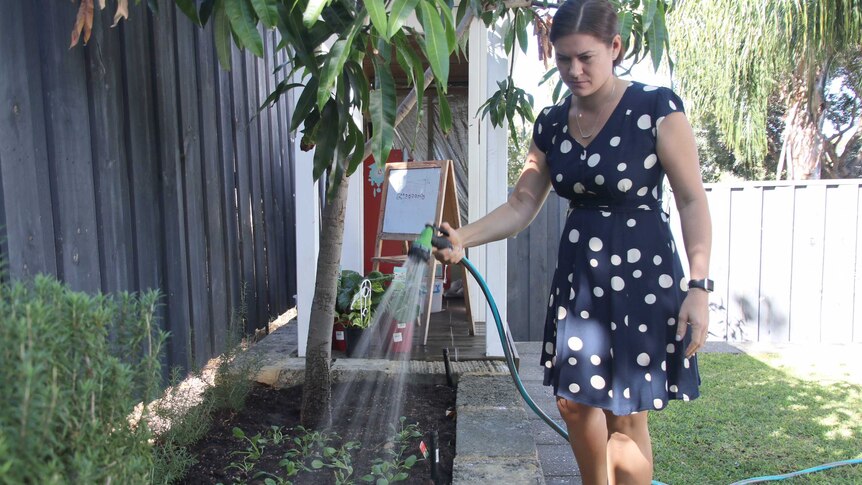 A woman stands in her backyard watering her garden with a hose.