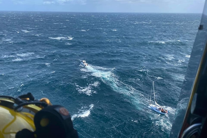 A yacht being towed by a small boat, as seen from a helicopter.