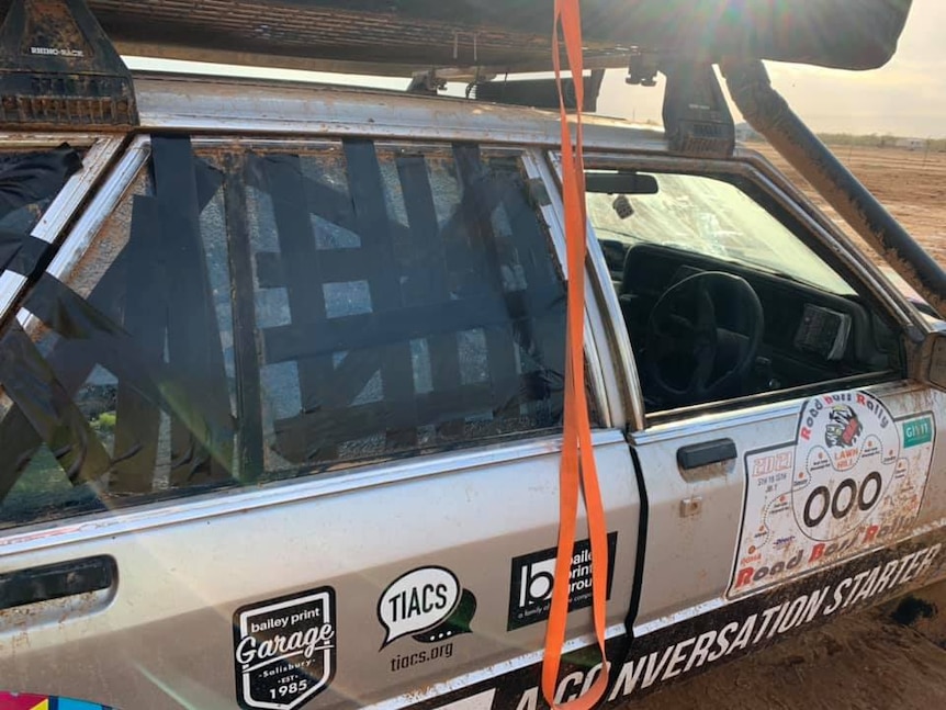 A muddy car with black tape over the broken back window.