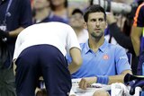 A trainer looks at the injured arm of Novak Djokovic