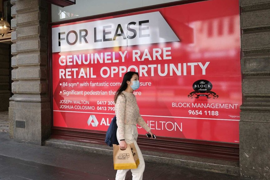 A woman in a face mask walks past a shop that is for lease in Melbourne's CBD.