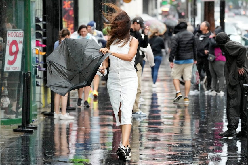 A woman tries to fix her broken umbrella while walking.