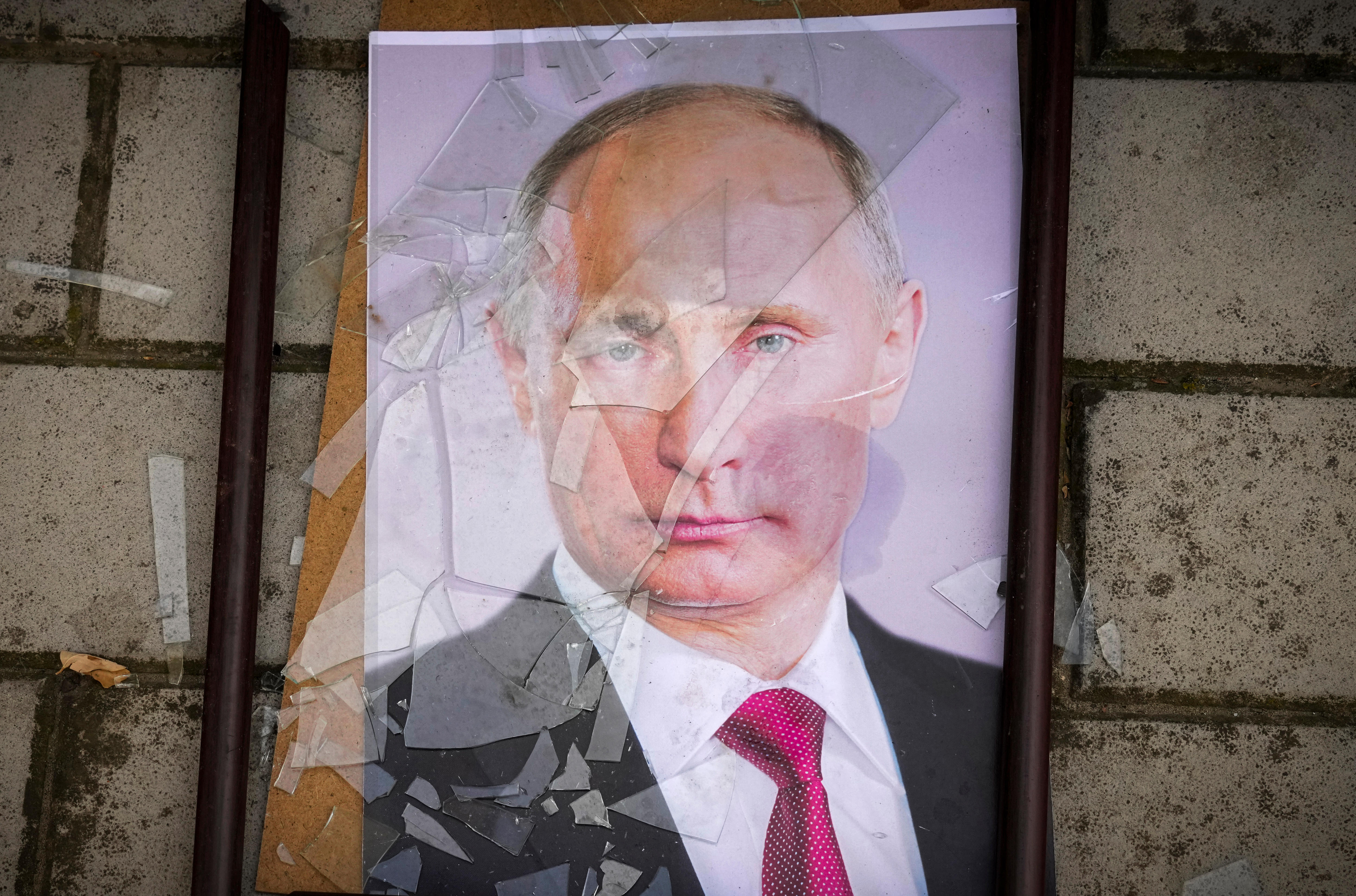 A framed portrait of Putin lies on the ground, the glass shattered across his face