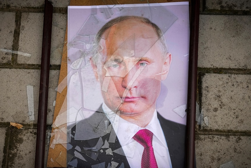 A framed portrait of Putin lies on the ground, the glass shattered across his face